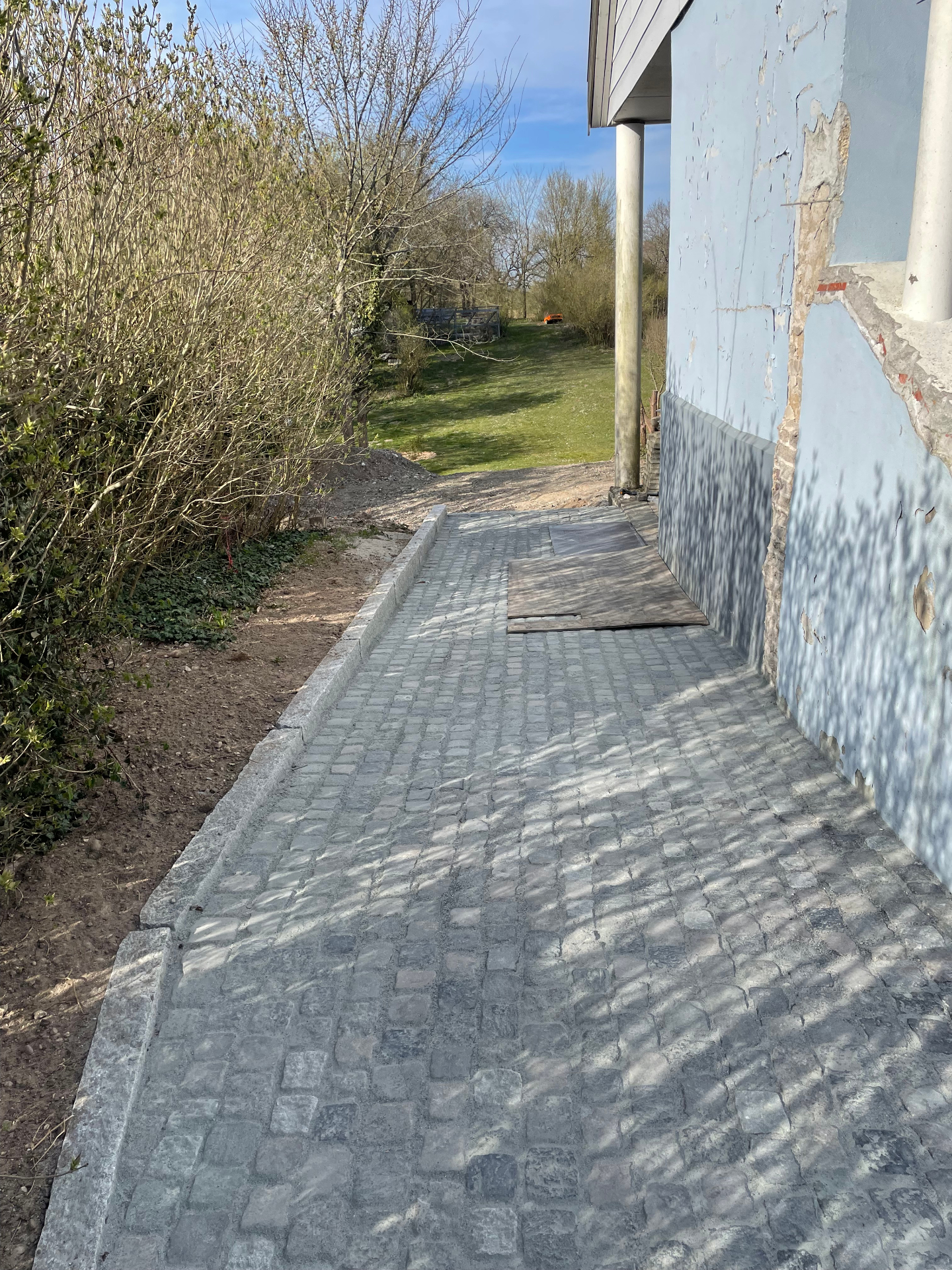Færdig stengangsti i mørke munkesten med kantsten langs et lyseblåt hus